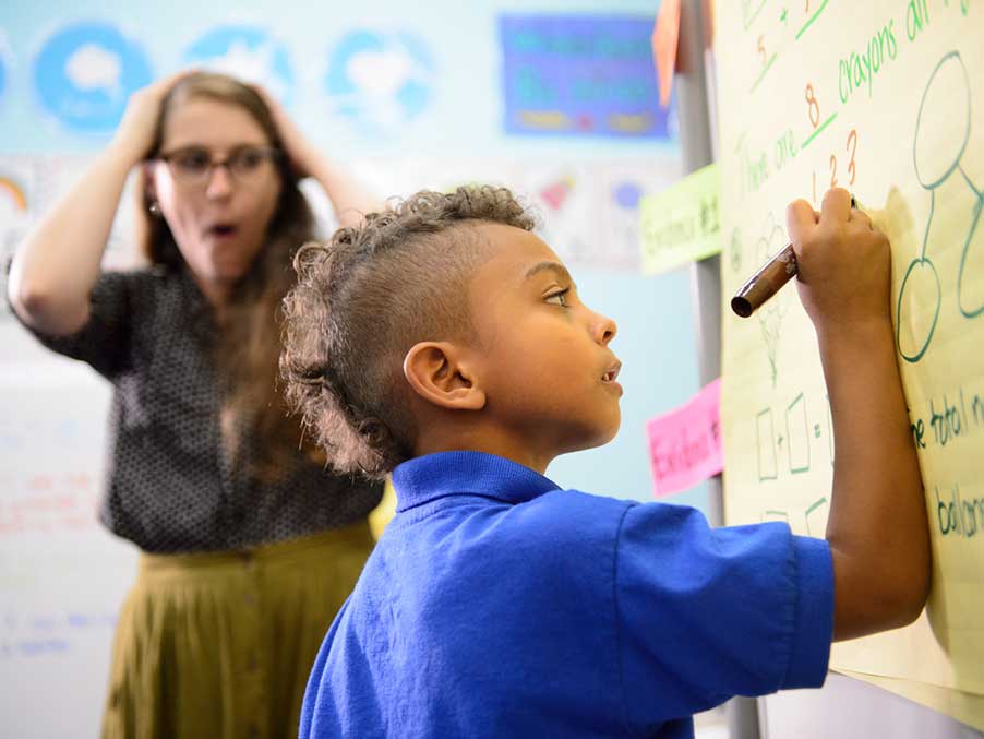 young boy writing on a white board in a class